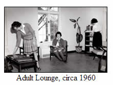 Three women in a 1960s lounge: one arranges magazines on a table, another sits reading in a chair, and a third looks at a shelf. Large window and a tall plant are in the background.