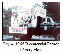 A truck decorated as a library float drives in a parade. People sit and read on the float, with large signs promoting reading. Banner reads Our Goal: Everybody Reading. Caption reads: July 4, 1965 Bicentennial Parade Library Float.